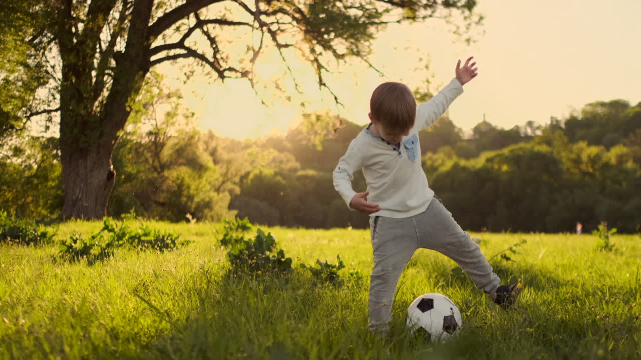 en cámara lenta el niño juega graciosamente con una pelota de fútbol en un prado al atardecer