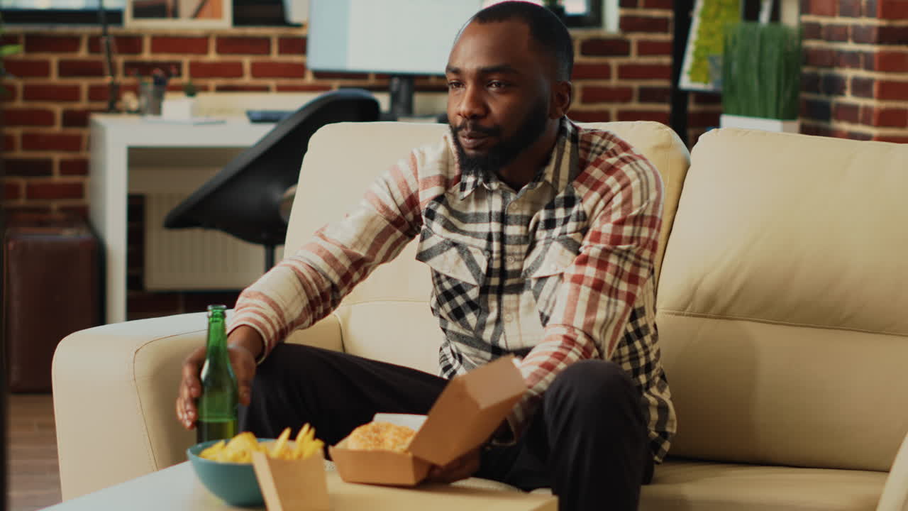 Modern guy eating cheeseburger with fries from takeout