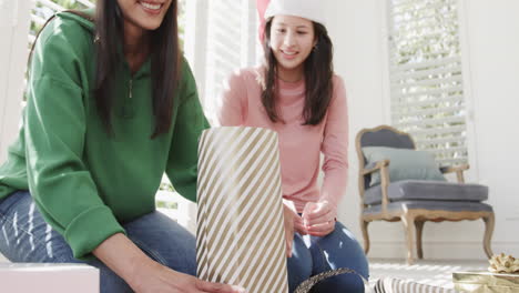 happy biracial mother and adult daughter wrapping christmas gift at home, copy space, slow motion