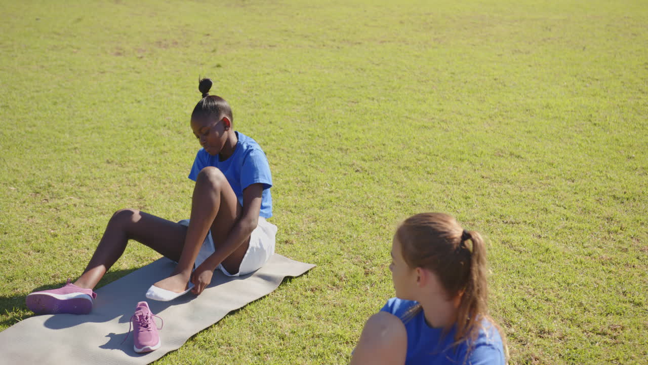 In school, girls sitting on grass putting on shoes during outdoor activity