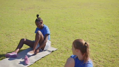 in school, girls sitting on grass putting on shoes during outdoor activity