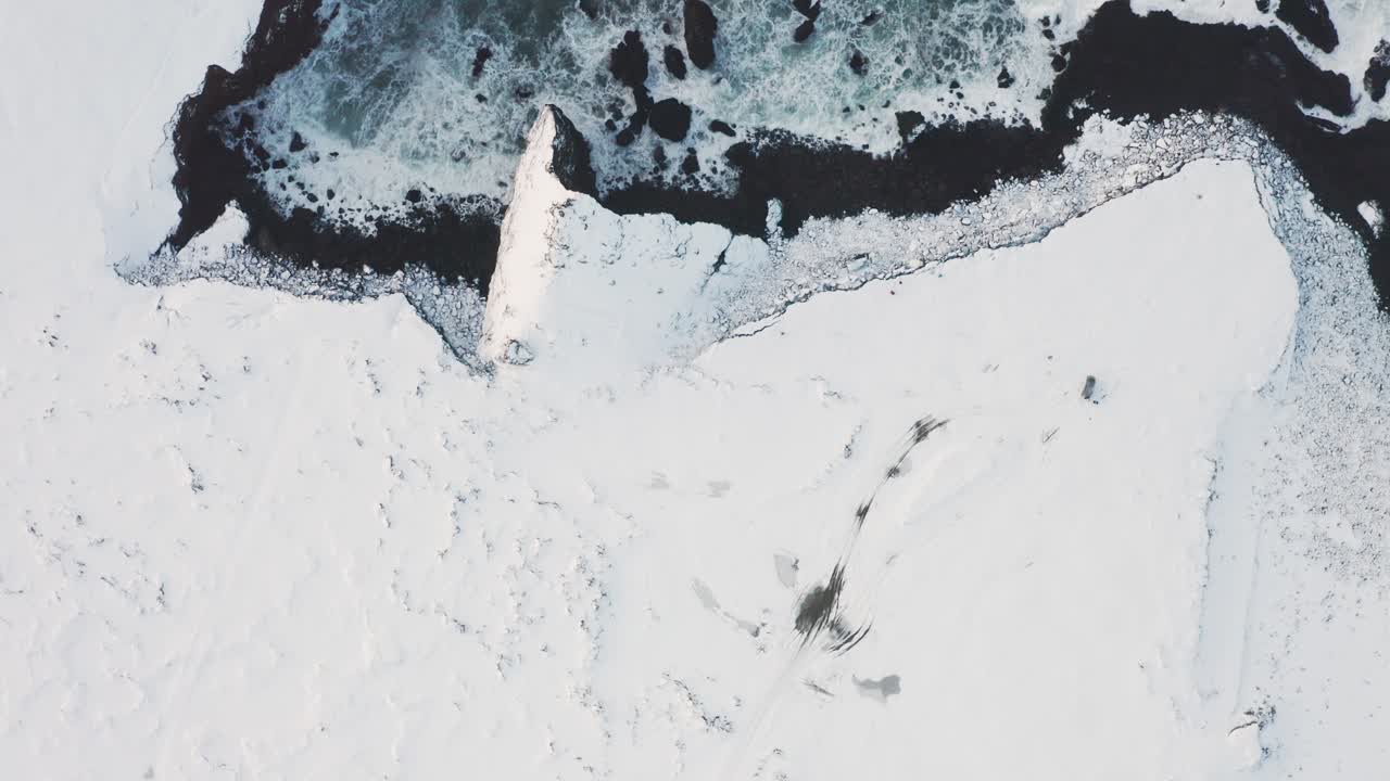 una hermosa toma de drones de la playa negra en islandia muestra las altas olas del mar y el clima nublado mientras la nieve cubre parte de la arena negra