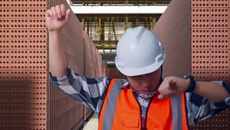 close up of asian male engineer with safety helmet screaming goal and dancing celebrating with red brick packed in stacks are stored