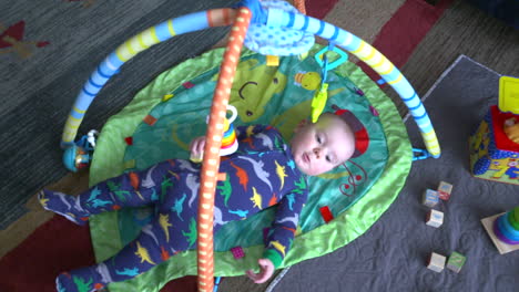 cute baby boy looking at colorful toys in his baby gym