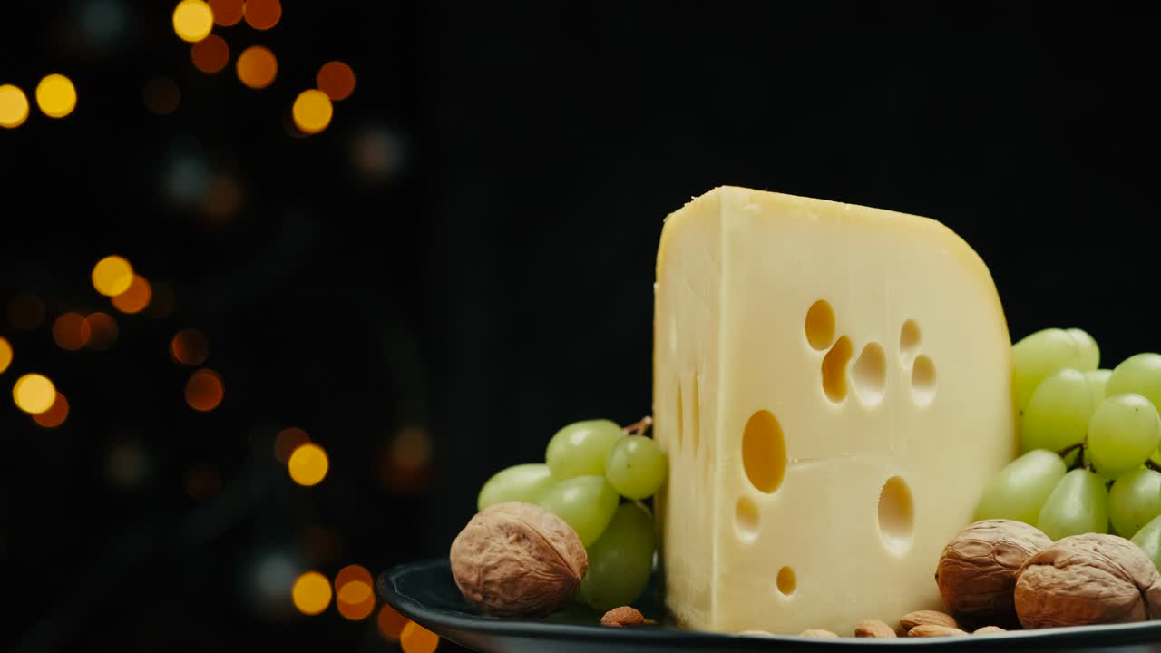 parte cerrada de la cabeza de queso duro medio edam gouda parmesán en tabla de madera, con nueces y uvas girando en el plato