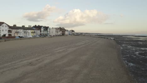 Flight-across-a-UK-beach-at-low-tide-in-the-Autumn,-beach,-housing-and-clouds