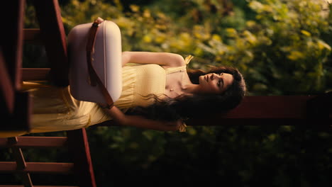 beautiful young brunette woman on balcony in yellow dress, cooler box, cinematic warm natural lighting, forest background, slow motion establishing shot, vertical