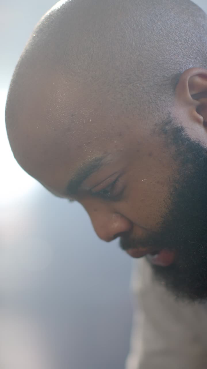 Vídeo vertical: Homem africano com cabeça raspada e barba, pálpebras tremendo, abrindo os olhos e se acomodando no quarto.