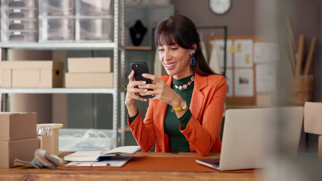Imprenditrice sorridente mentre usa lo smartphone alla sua scrivania