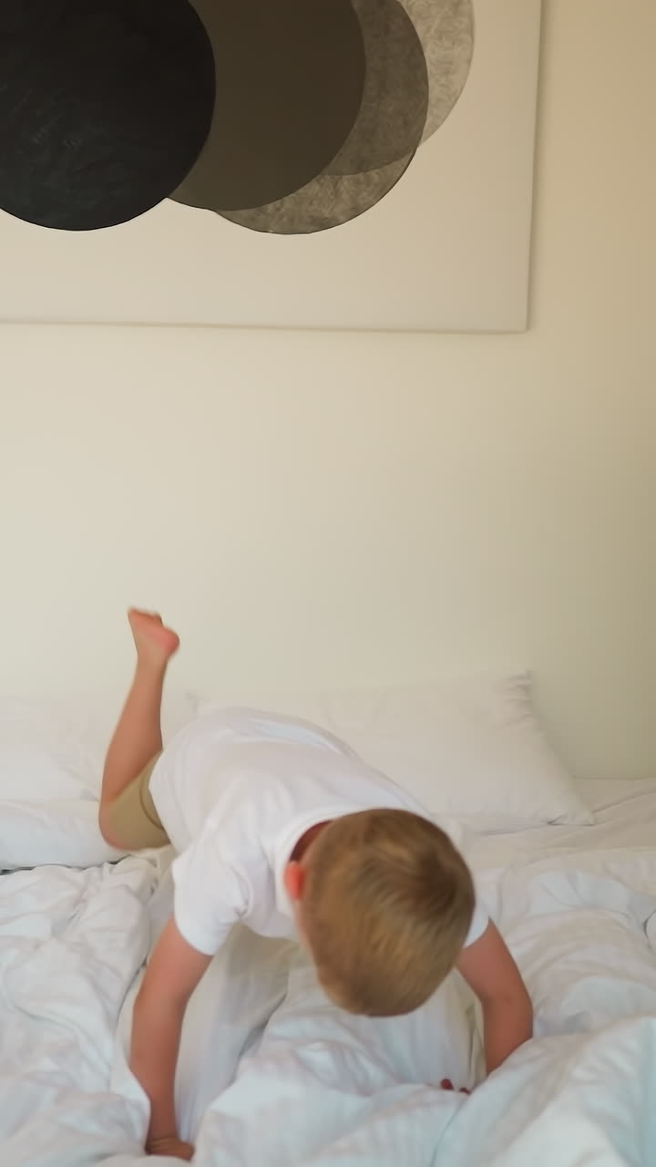 아이가 글램핑에서 담요와 함께 침대에 뛰어들고, 사랑스러운 어린 소년은 텐트 호텔 침실에서 부드러운 플레이드에 떨어집니다. 활동적인 아이는 캠핑에서 재미있습니다.