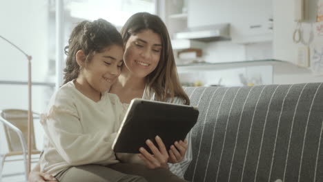 little girl watching video on digital tablet with mom at home