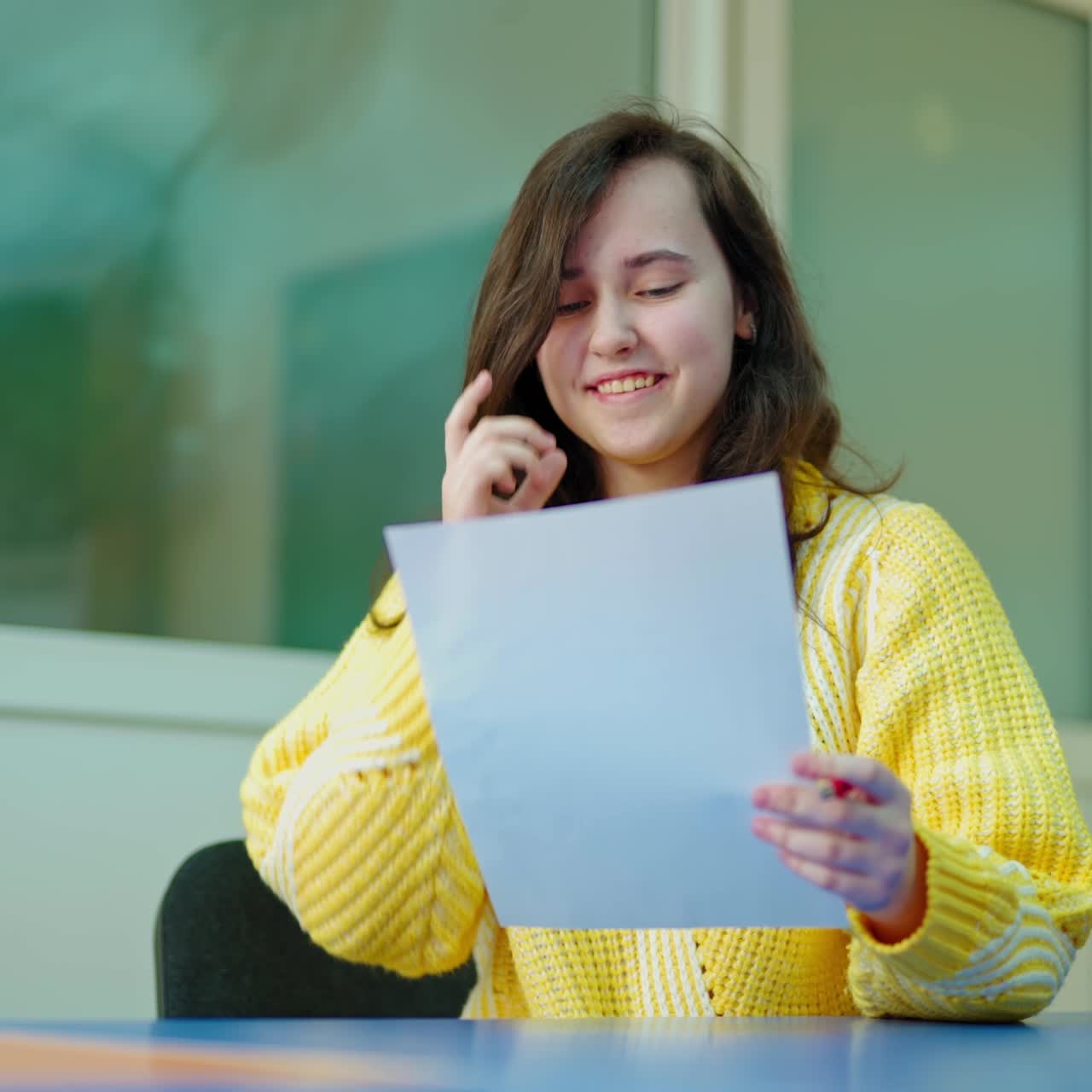 Smiling student studying at school. Beautiful teenage girl holds a paper and throwing it away. Portrait of a school girl sitting in the classroom. Education concept.