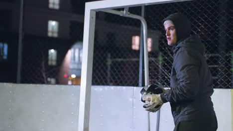 goalkeeper prepares to kick soccer ball during night practice near goalpost, with dimly lit residential buildings in background athlete demonstrates technique under stadium lighting