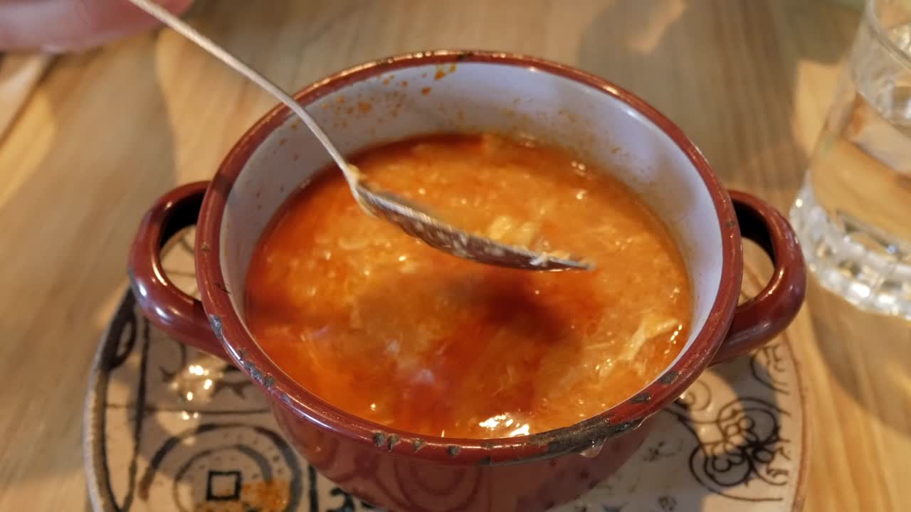 A hand lifting the lid of a clay pot revealing a traditional Castilian soup