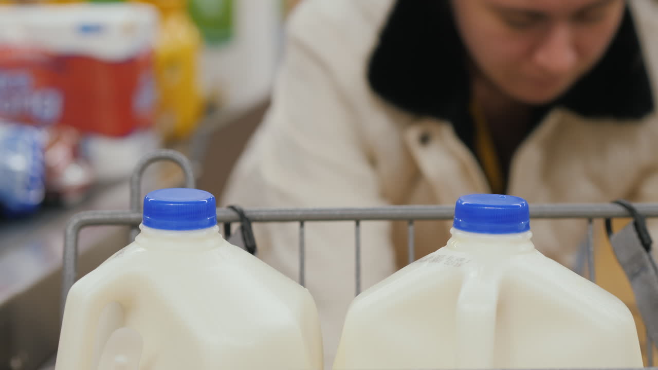 el cliente descarga las compras del carro y las coloca en la cinta en la caja registradora. grandes botellas de leche en primer plano