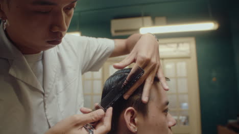 male barber trimming hair of a client in barbershop
