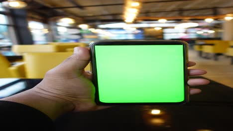 person holding a green screen smartphone in a cafe