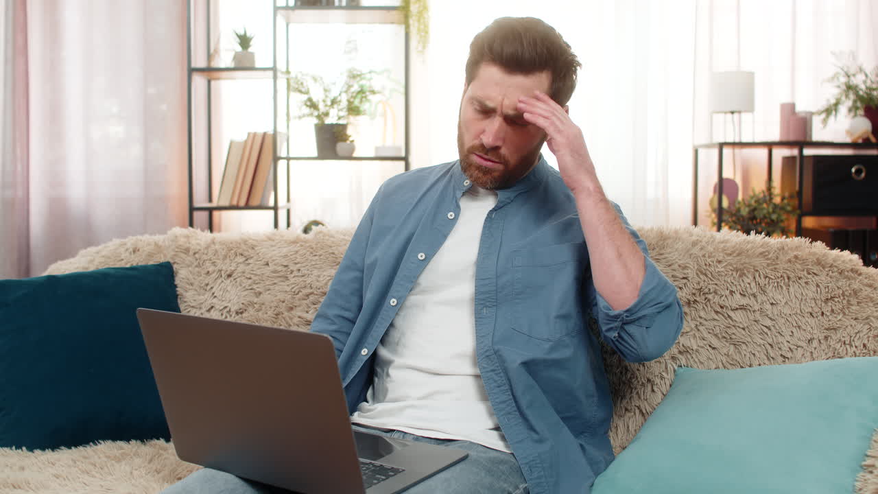 Young man upset holding head while looking at laptop screen receiving bad news or seeing big bill