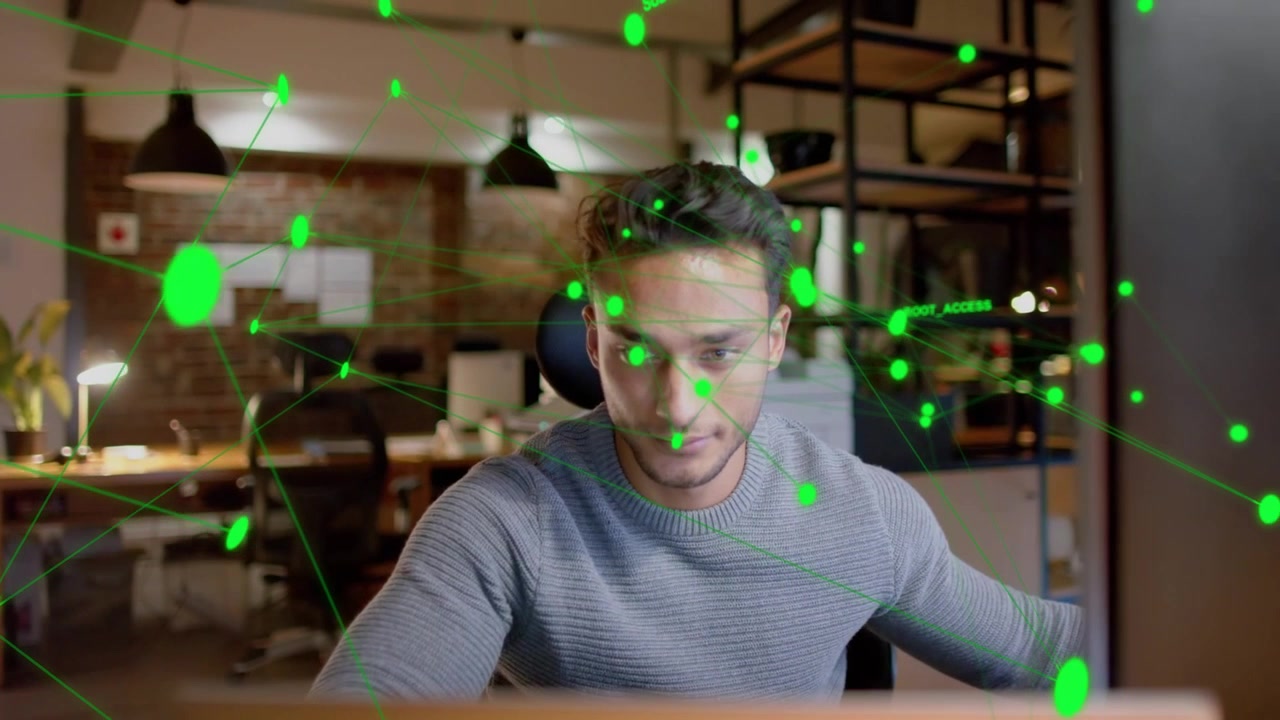 Man at desk reaching to input, initiating tech feed and overlaying green node network across face