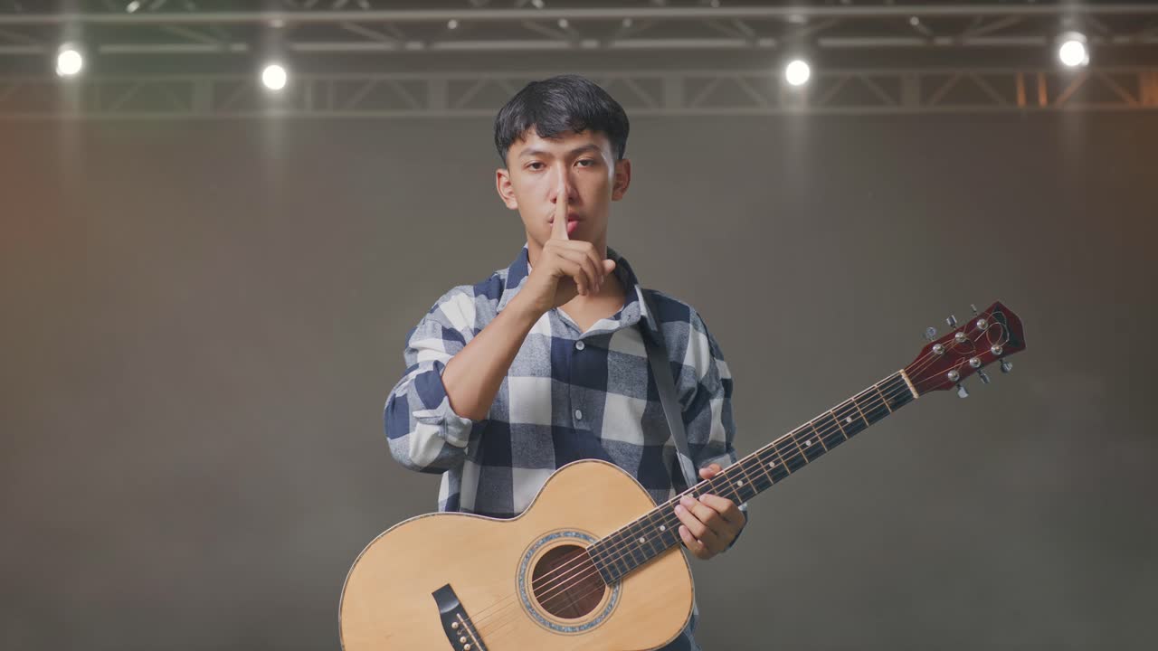 기타 를 들고 무대 에 서 있을 때 침 의 몸짓 을 하는 아시아 청소년