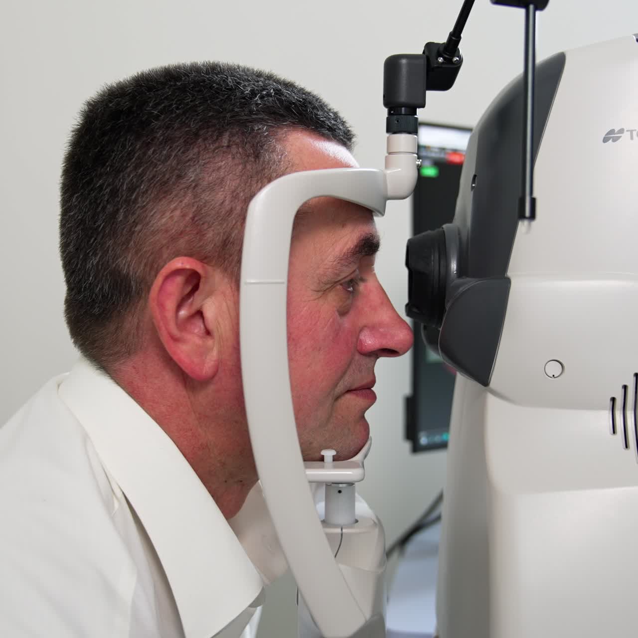 Adult man sits at the apparatus for eyesight examination. Patient looks straight ahead into device binocular. Side view