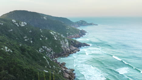 Vista-Aérea-De-Las-Olas-Del-Mar-Y-La-Puesta-Del-Sol-En-El-Océano-Una-Fantástica-Costa-Rocosa,-Praia-Da-Joaquina,-Florianópolis,-Santa-Catarina,-Brasil