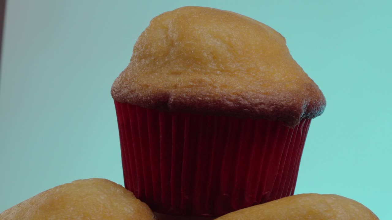 Close-up of a golden muffin in a red liner, set against a blue background