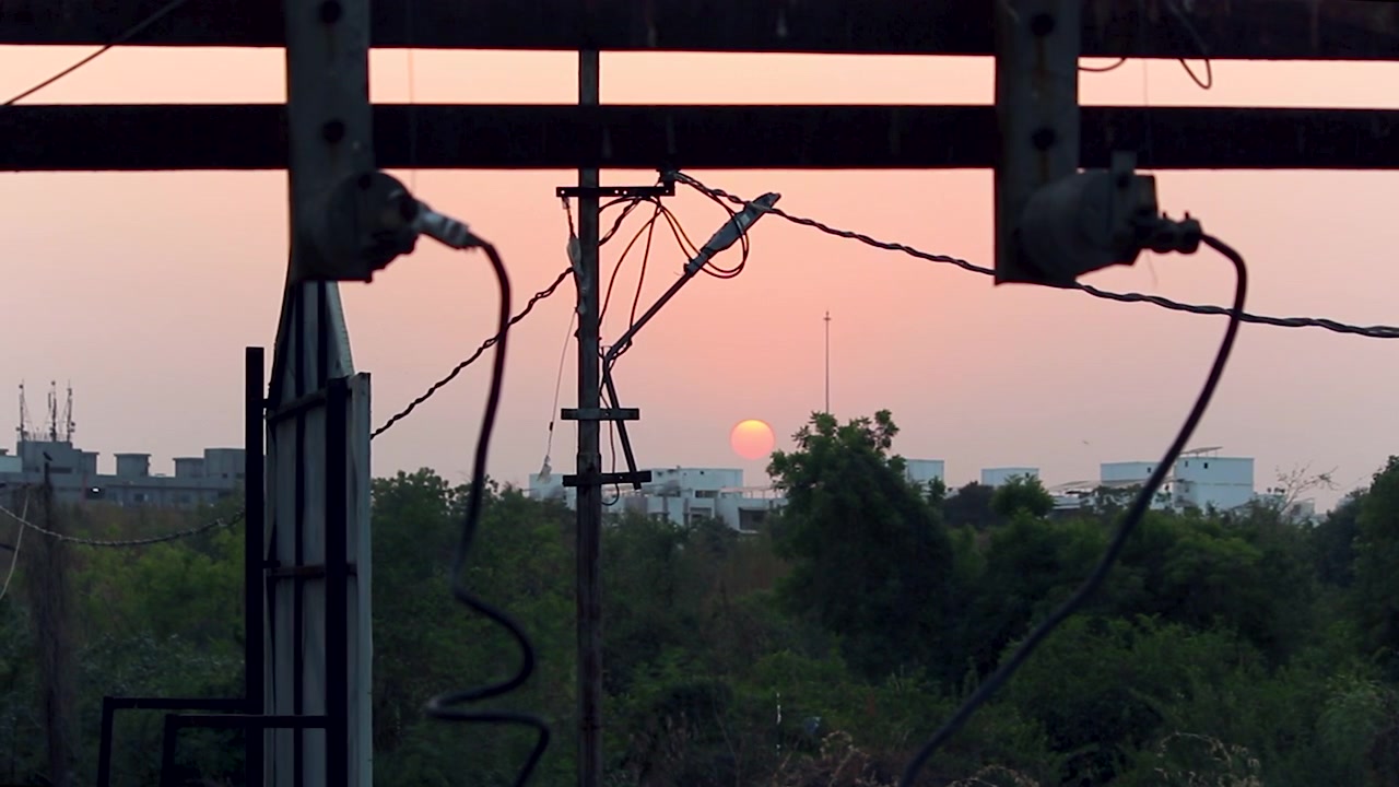 電線と都市構造物を通して見る雰囲気のある夕焼けの景色。都市生活、インフラ、エネルギー関連テーマ、産業の物語性、映画のような夕景に最適です。