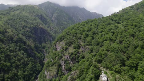 Remote-church-in-mountain-forest,-Livo-Valley,-revealed-by-backward-aerial