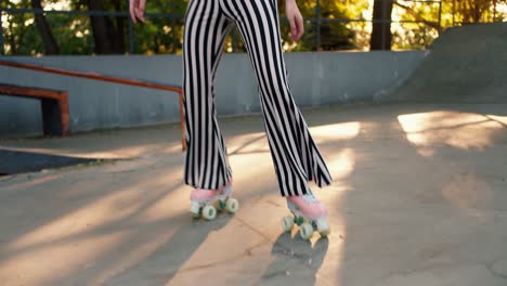 Portrait-of-a-girl-with-a-short-haircut-in-a-purple-top-and-striped-pants-rides-on-pink-roller-skates-in-an-outdoor-skatepark-in-summer