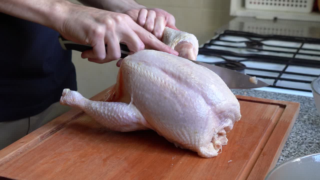 Una persona in cucina taglia le cosce di un pollo intero con un coltello affilato.