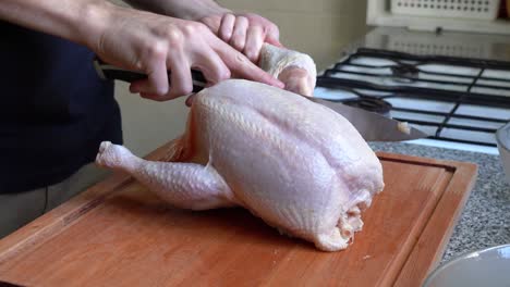 person in the kitchen with whole chicken cutting thighs using sharp knife