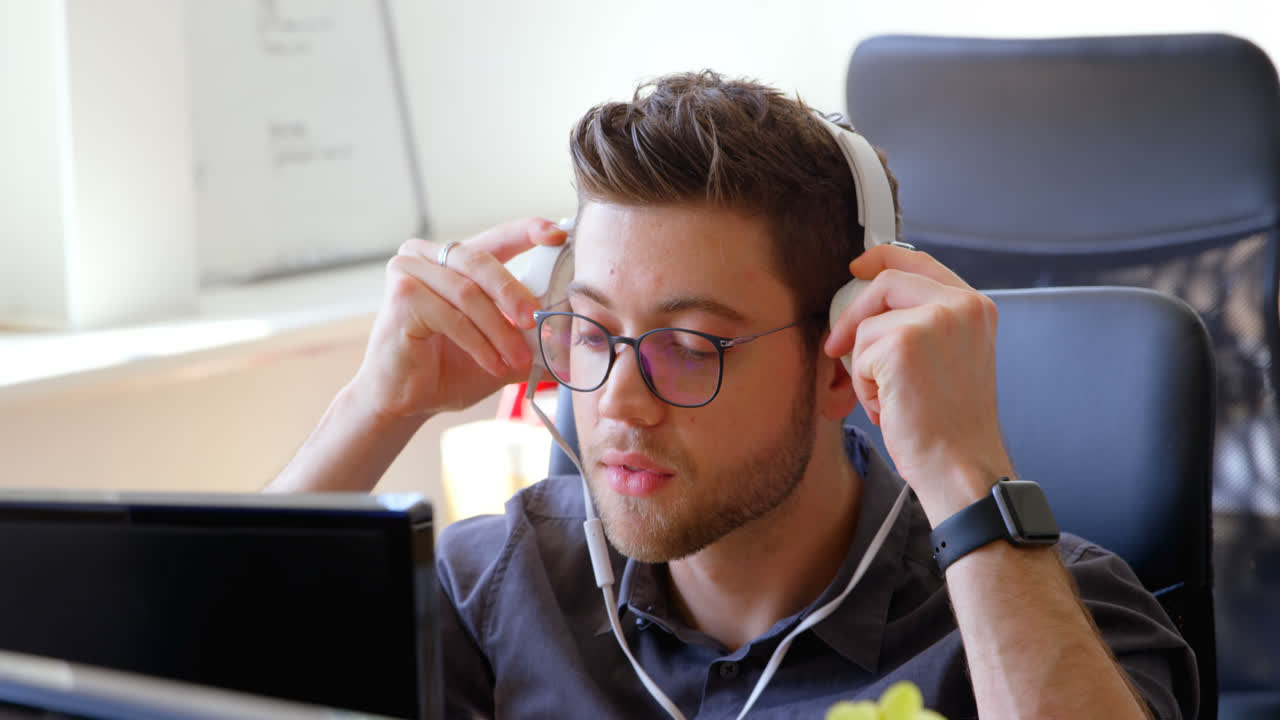vista frontal de un joven empresario caucásico con auriculares y trabajando en un escritorio en una oficina moderna 4k