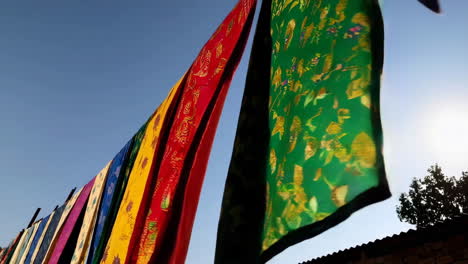 vibrant patterned fabrics drying under a clear blue sky with sun flare