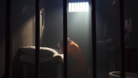 inmate kneeling beside bed during prayer in prison cell