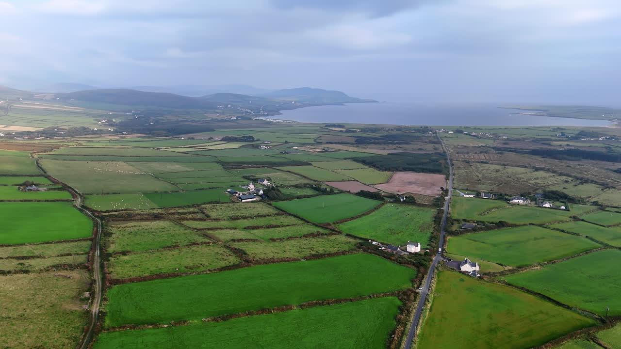 Huge vast valley in the mountainous area is divided into the separate farmlands. Beautiful landscapes of Ireland with waterscape at backdrop. Aerial perspective.