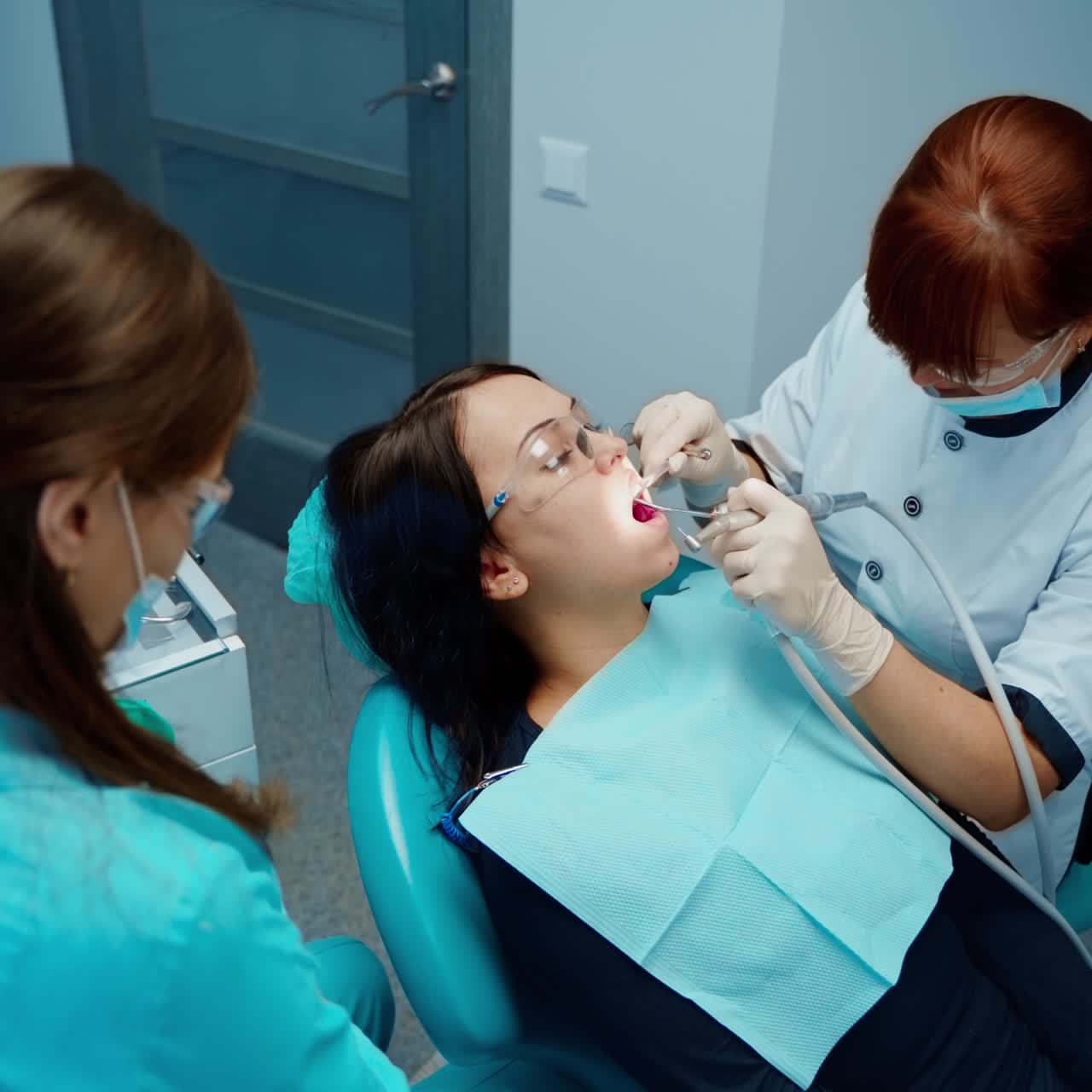 Professional female stomatologist at work. Young woman sitting in dental chair during teeth treatment. Dentist uses modern medical equipment in dentistry. Top view.