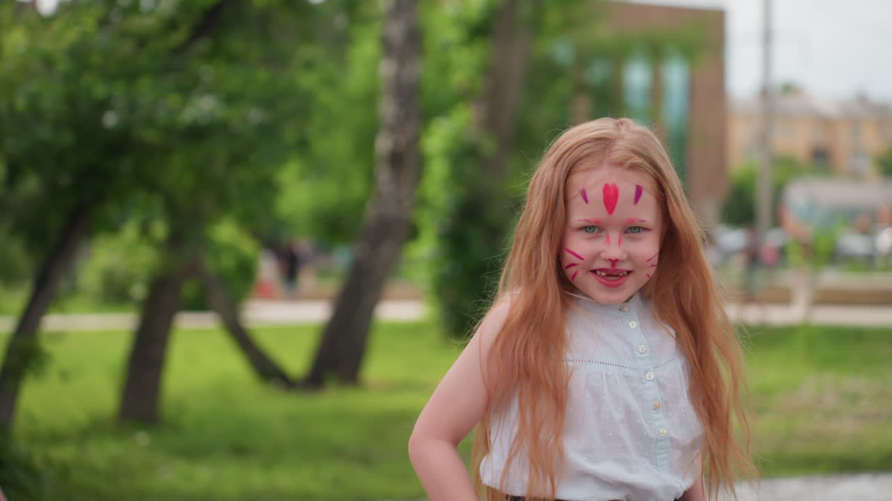 young girl with face paint smiling playing in park, long red hair flowing, sunlight filtering through trees, blurred green background creating soft depth, joyful expression of carefree childhood