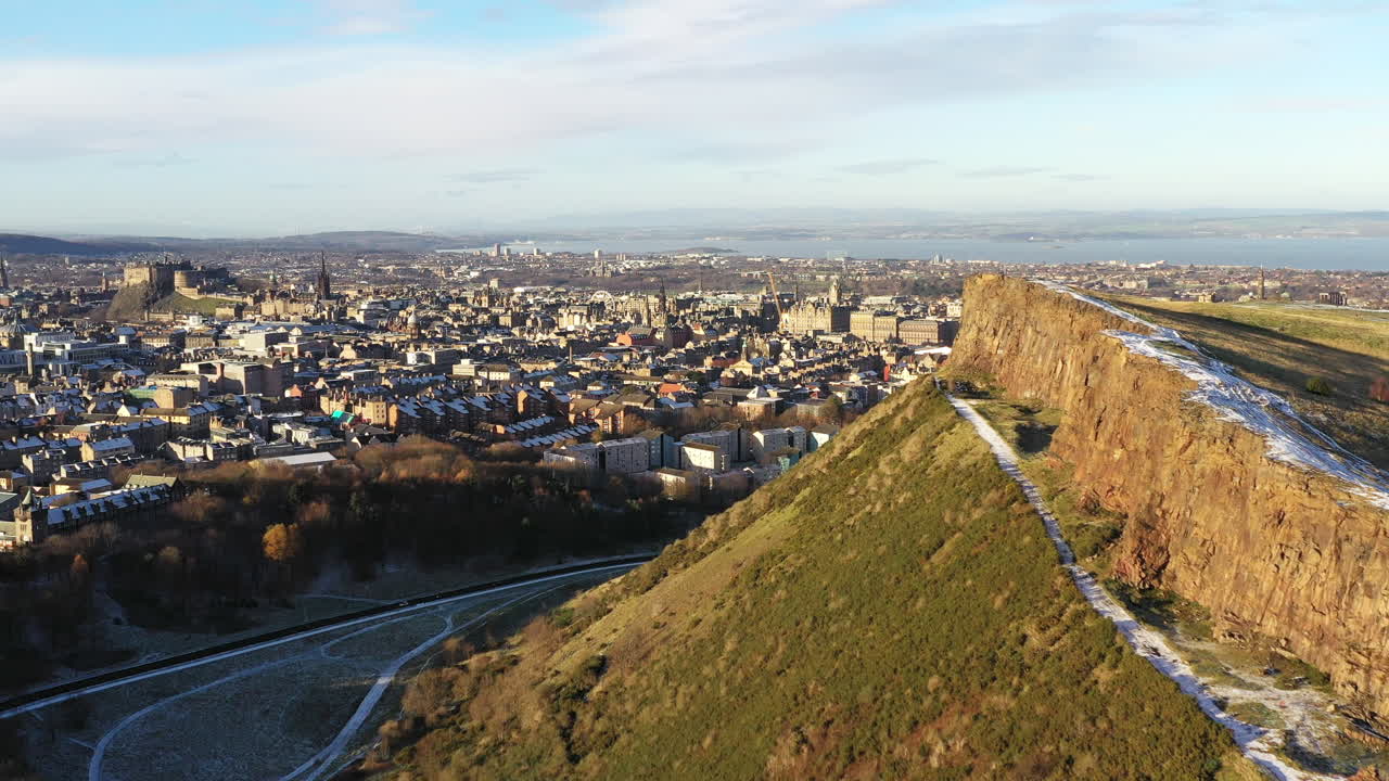 Aerial shot of Edinburgh in the snow, with Arthurs's seat and Salisbury crags in the foreground, and Edinburgh Castle in the background