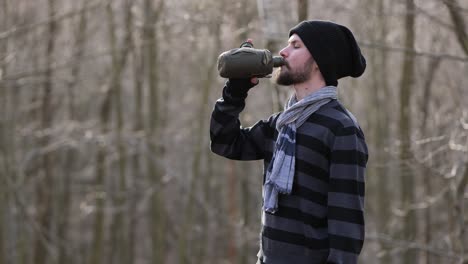 Portrait of male hiker drink water from canteen on trip in forest on autumn day