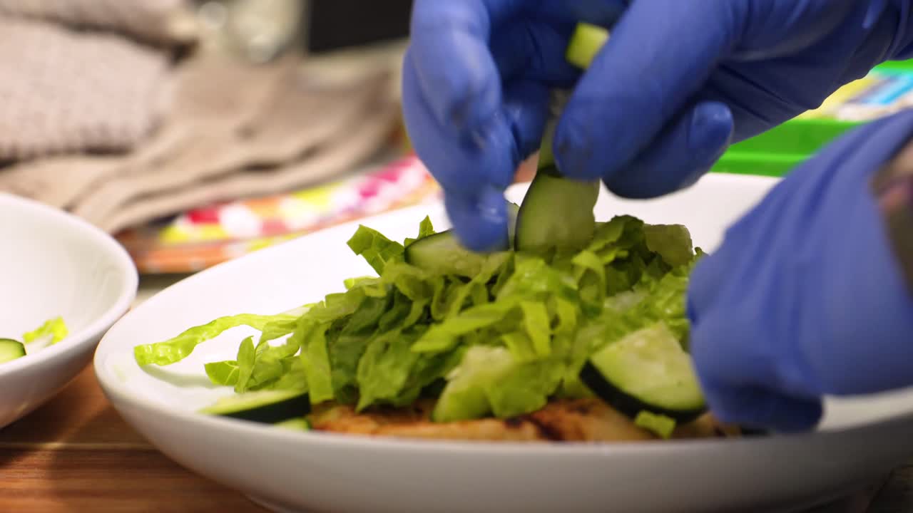 Putting Slice Cucumber On Top Of Pita Vegetable Salad While Wearing Blue Rubber Gloves - Closeup Shot