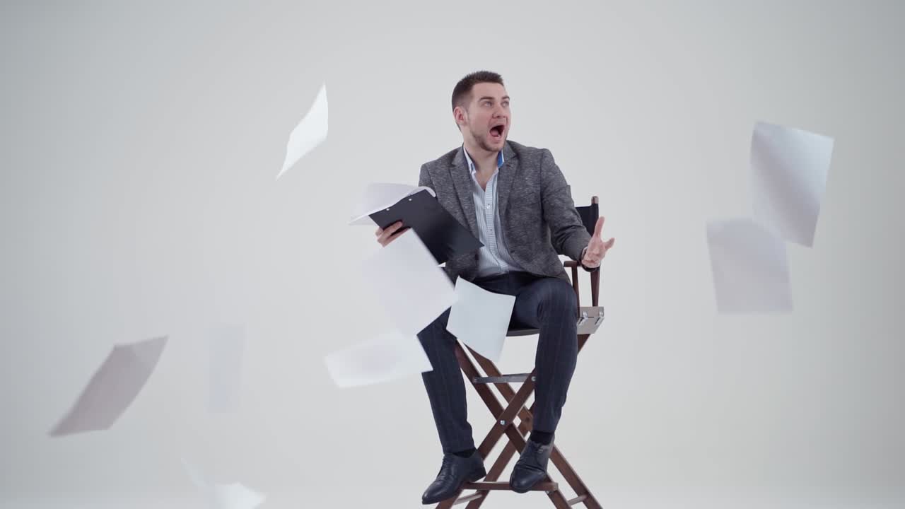 Businessman in a chair shouting. Many papers are flying in the studio and a man in suit with opened mouth. Slow motion.