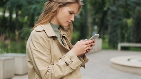 upset caucasian female student using smartphone outdoors.