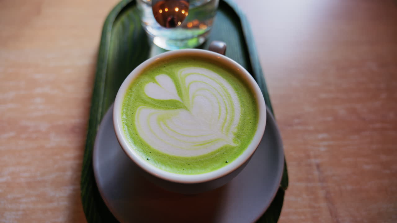 Close up of a matcha latte and a glass of water on a little green tray on a table at a cafe