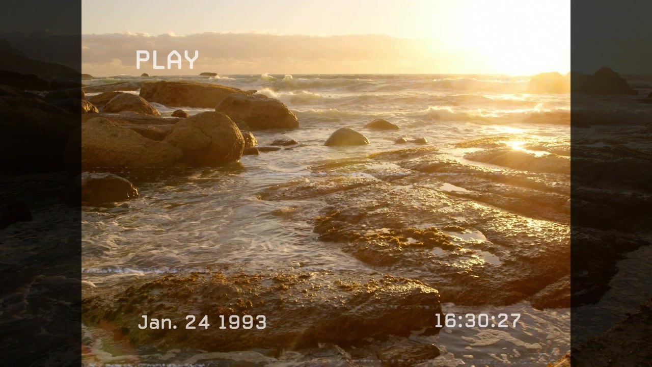 Fixed camera recording rocky shore with timecode updating and PLAY overlay waves lapping at sunset