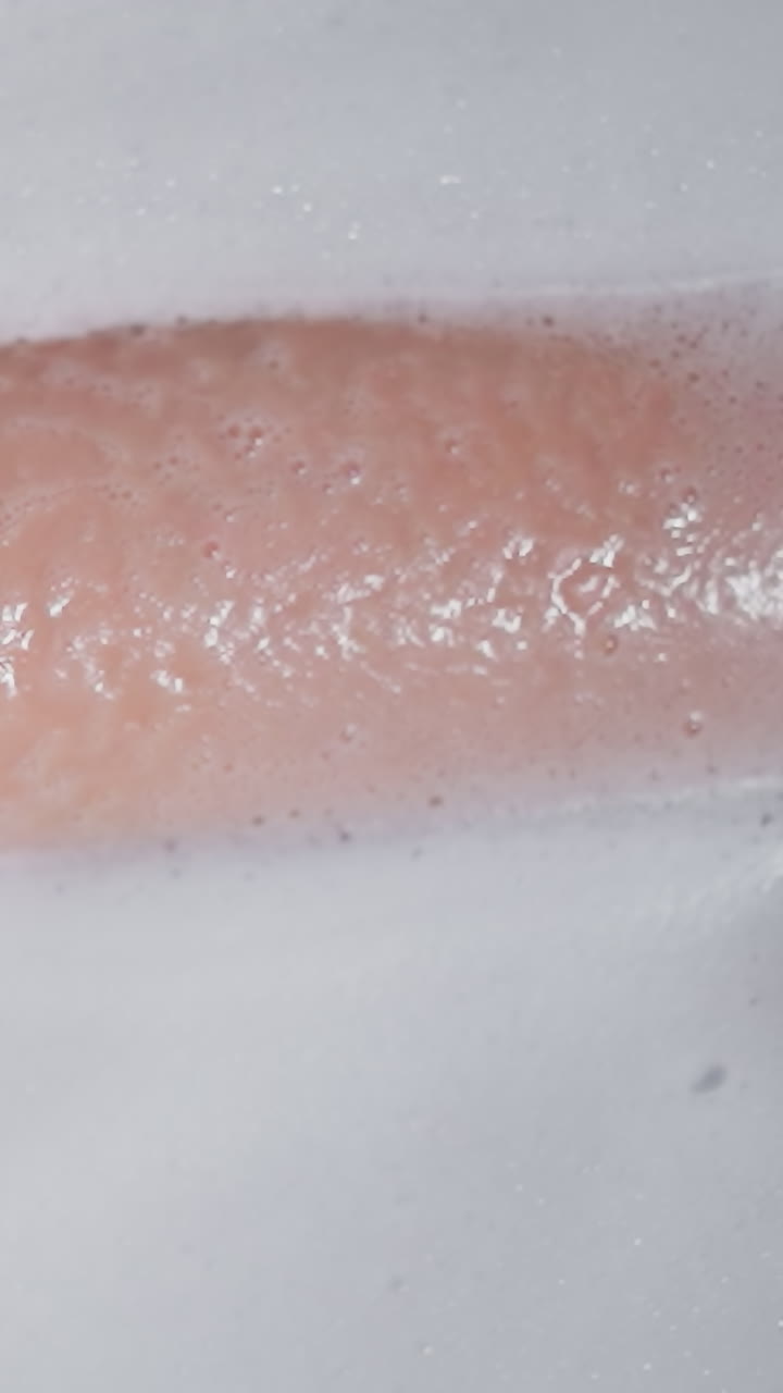 mujer con la pierna en el agua espumosa de la bañera de primer plano. dama elegante toma un baño relajante con productos para el cuidado de la piel en casa. mujer joven disfruta de la rutina de cuidado corporal