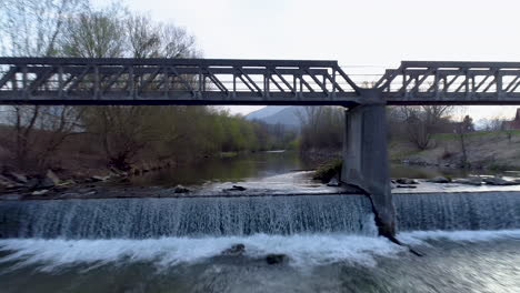 Disparo-Rápido-Y-Cercano-De-Drones-Volando-Hacia-Atrás-A-Través-De-Un-Puente-Sobre-Un-Río,-4k-Uhd