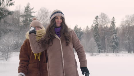 Vista-Frontal-De-Una-Madre-Y-Una-Hija-Con-Ropa-De-Invierno-Jugando-A-Tirar-Nieve-En-Un-Bosque-Nevado