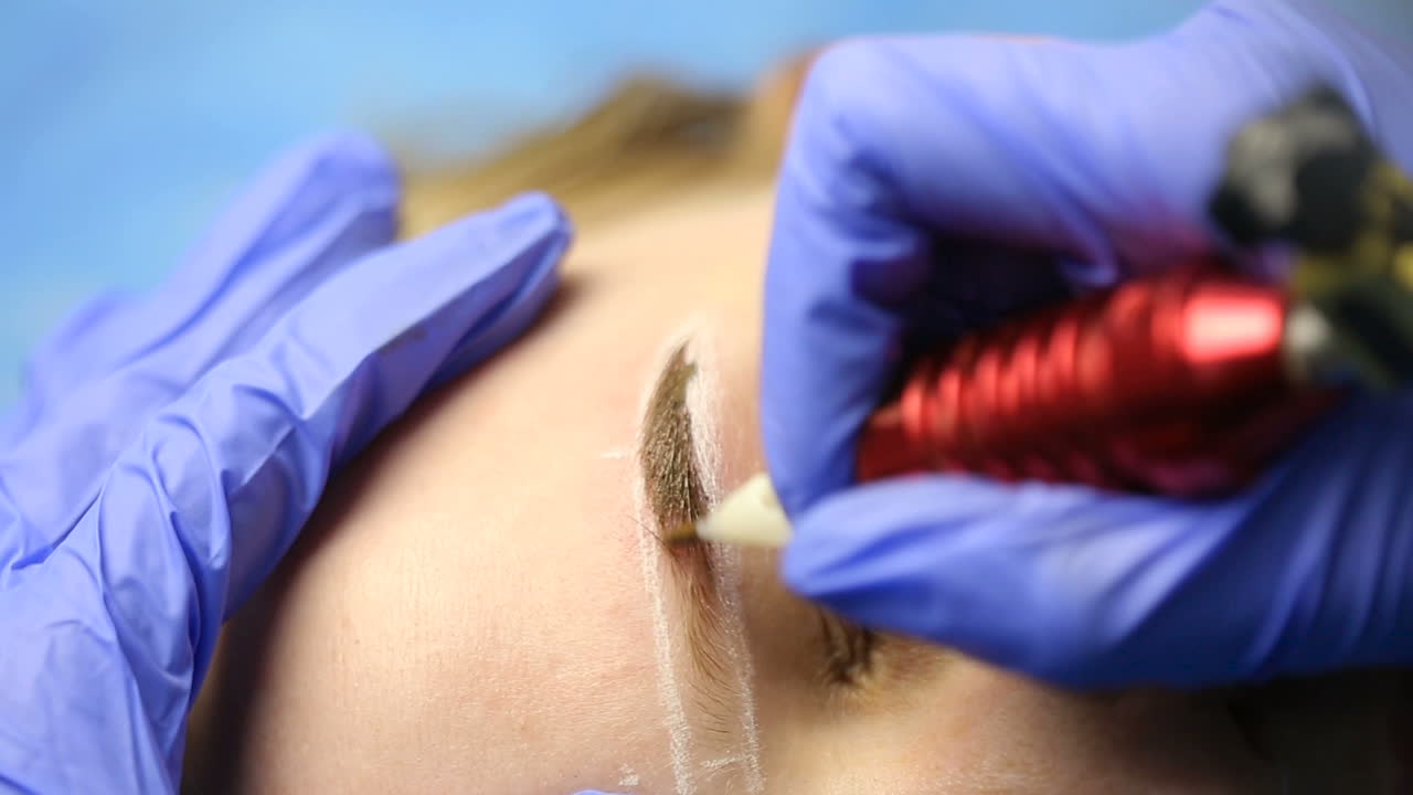 Beautician doing eyebrow tattooing for female face