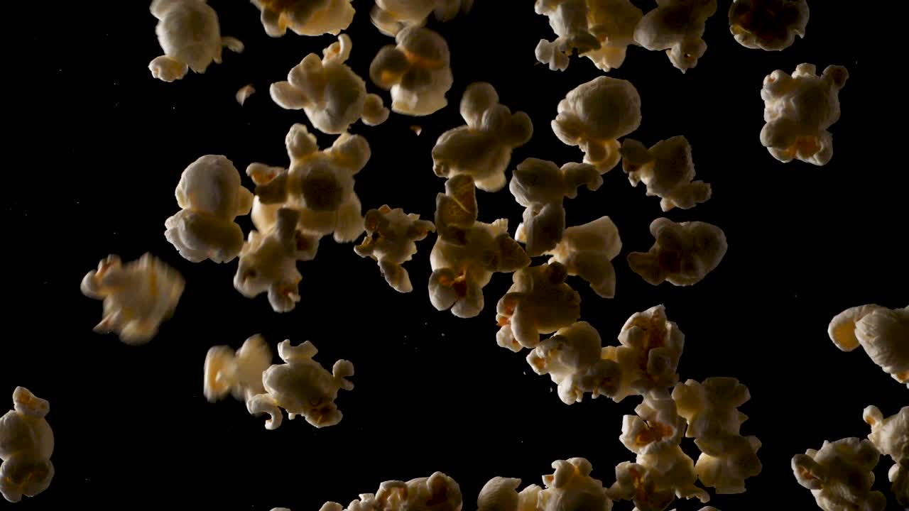 큰 팝콘 더미가 격리된 검정색 배경을 가진 스튜디오의 카메라에서 느린 동작으로 떨어집니다.